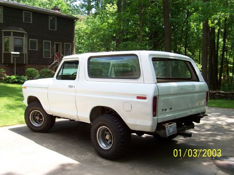 1979 Ford Bronco - A white Ford Bronco is viewed from the rear three-quarter angle, parked on a concrete driveway in front of a house.