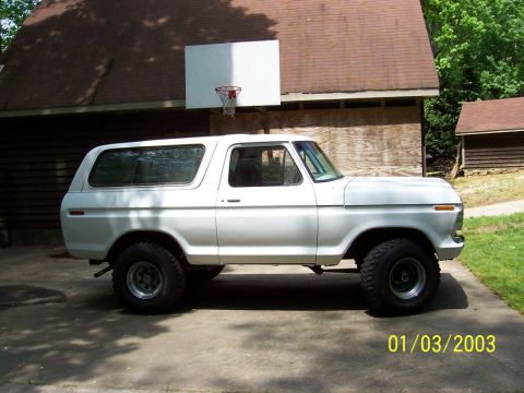 1979 Ford Bronco - A white 1978 Ford Bronco is parked on a concrete driveway next to a wooden building with a basketball hoop overhead.