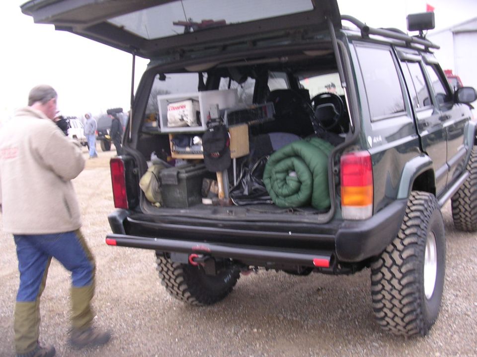 1995 Jeep Cherokee rear view with open tailgate, camping gear inside, and large off-road tires