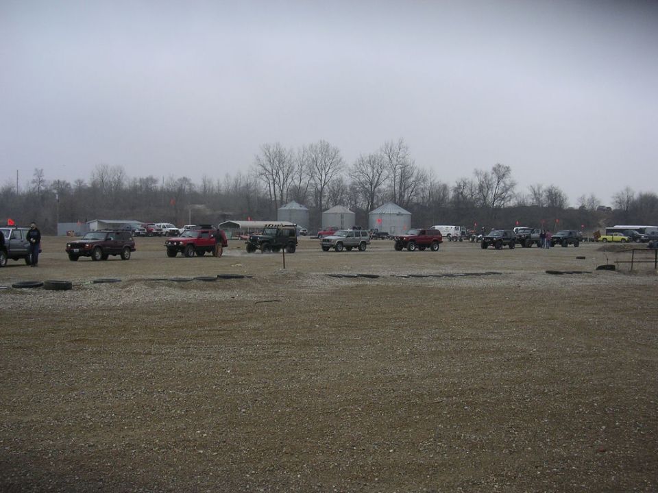 Several off-road vehicles parked in an open lot with silos in the background