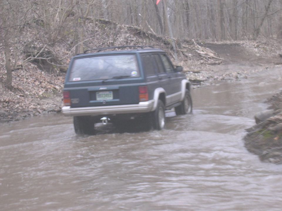 Rear view of a dark blue 1995 Jeep Cherokee driving through water
