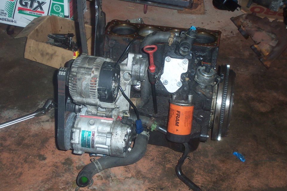 Engine assembly with alternator, AC compressor, and oil filter. Some boxes and tools are in the background