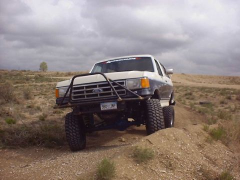 1988 Ford Bronco - Modified 1988 Ford Bronco tackling an off-road trail under a cloudy sky.