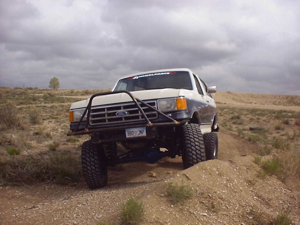 1988 Ford Bronco with custom bumper and lift kit on a dirt trail