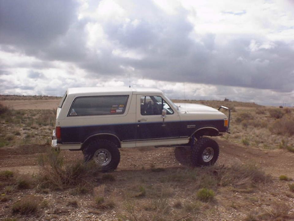 Two-tone white and dark blue Ford Bronco with lifted suspension and off-road tires on a dirt path