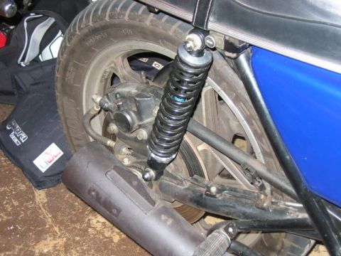 1985 Ford LTD Crown Victoria - Close-up view of a motorcycle's rear wheel, suspension, and exhaust system, with branded bags nearby.