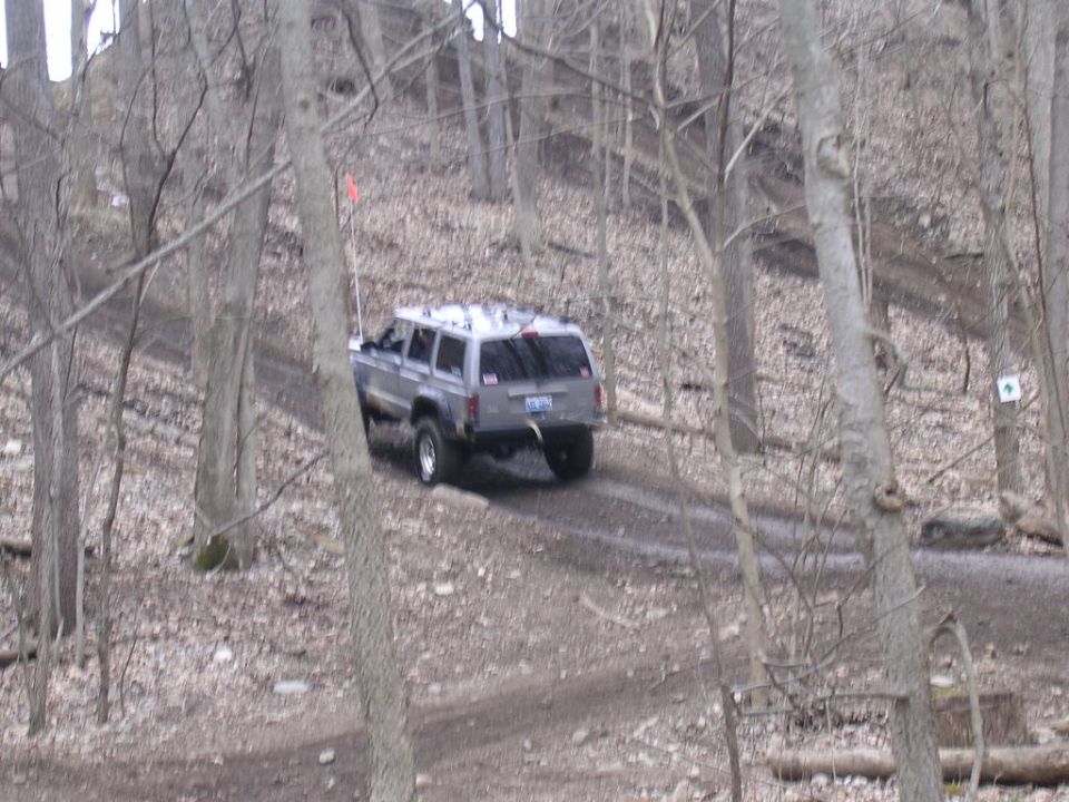 Gray 1995 Jeep Cherokee from rear view driving on a dirt road in woods