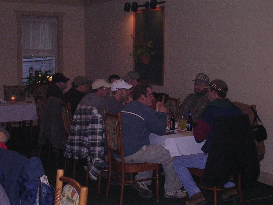 Several guys are sitting around a table in a dimly lit room. Some have hats on
