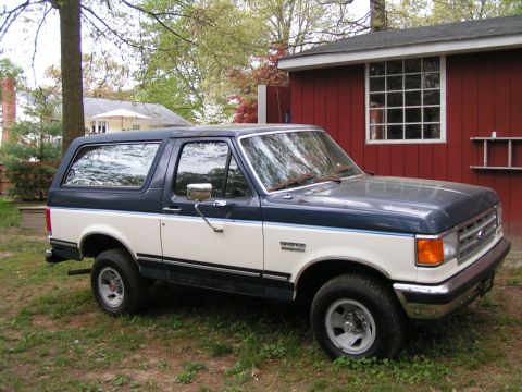 1987 Ford Bronco - This two-tone blue and white 1987 Ford Bronco is parked on a grassy lawn next to a red shed.