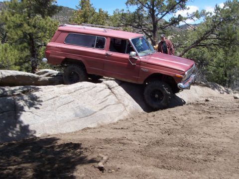 1991 Ford Bronco - A red Jeep Cherokee Chief navigates a rocky trail, demonstrating its off-road capabilities.