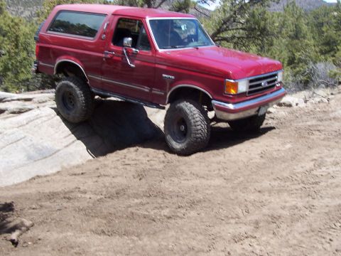 1991 Ford Bronco - 1991 Ford Bronco tackling a challenging off-road trail with steep inclines and loose dirt.