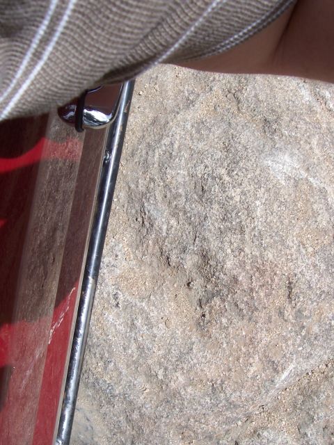 1991 Ford Bronco - A portion of a red vehicle's exterior, chrome trim, is shown against a textured, rocky surface.