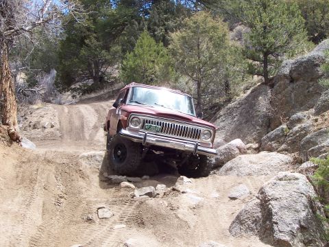 1991 Ford Bronco - A red Jeep Cherokee navigates a challenging rocky terrain on an off-road trail.