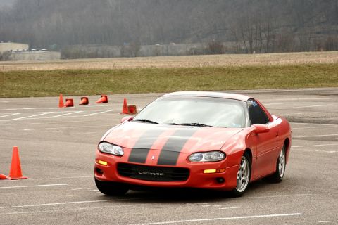 1999 Chevrolet Camaro - A red 1999 Chevrolet Camaro with black racing stripes navigates a course marked by orange cones.