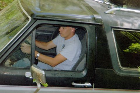 1988 Ford Bronco - A man is seen driving a dark-colored SUV, possibly a Ford Bronco, on a wooded road.