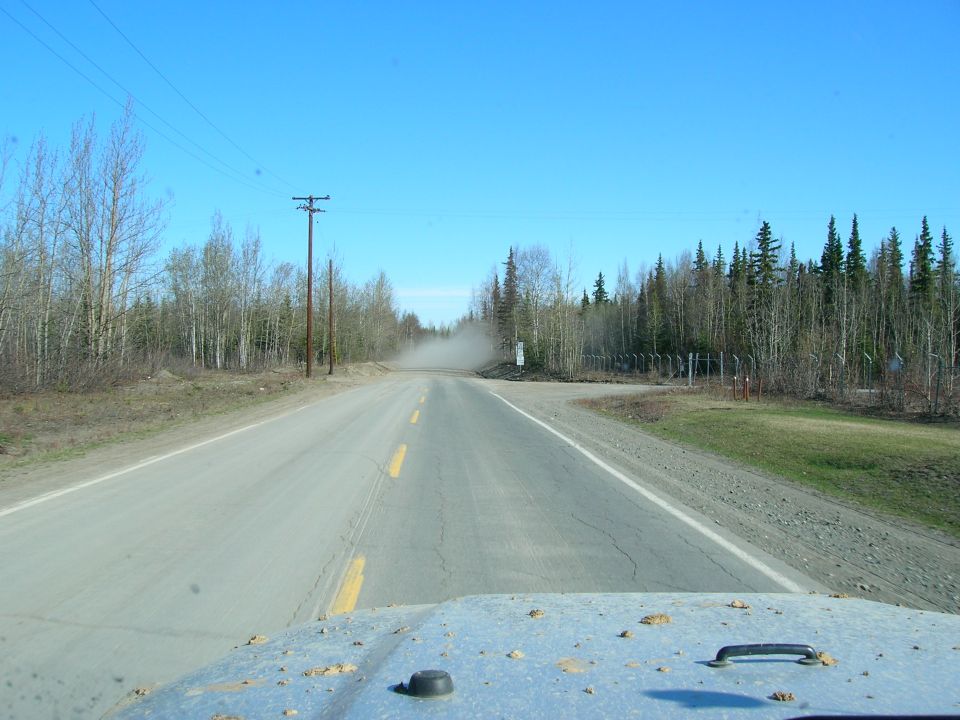 View from inside a Jeep looking at the hood and a dusty road ahead