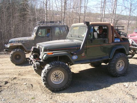 2003 Jeep TJ - Two Jeep Wranglers are parked on a dirt path, one green with a snorkel and the other covered in mud.