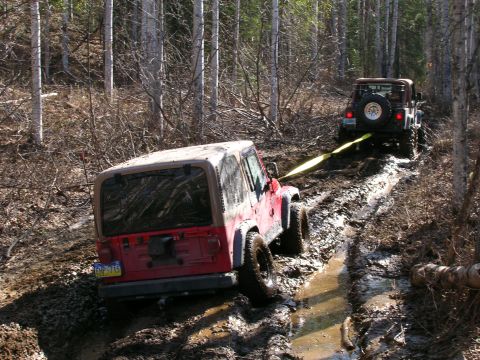 2003 Jeep TJ - Two Jeeps navigate a muddy trail, one assisting the other.