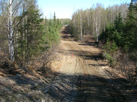 2003 Jeep TJ - A red SUV navigates a rough, uphill dirt track surrounded by dense trees.