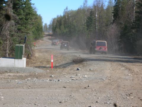 2003 Jeep TJ - Multiple Jeeps travel down a dirt road, kicking up dust in a wooded area.