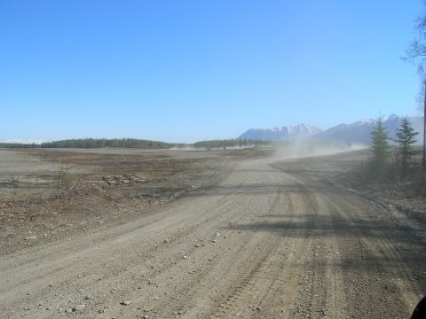 2003 Jeep TJ - A vehicle travels down a dusty dirt road, leaving a trail of dust in its wake under a clear blue sky.