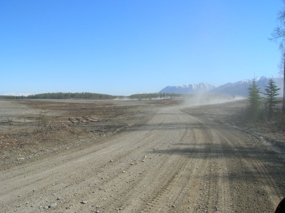 dirt road kicking up dust with mountains and trees in distance