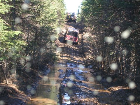 2003 Jeep TJ - Two off-road vehicles are seen on a challenging muddy trail in a wooded area.