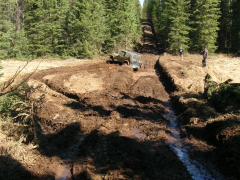 2003 Jeep TJ - An off-road vehicle navigates a challenging muddy terrain with onlookers observing the difficult passage.