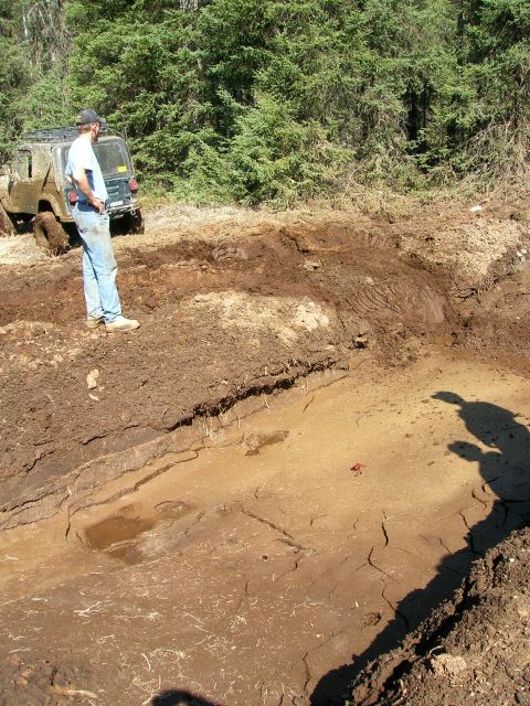 2003 Jeep TJ - A Jeep is stuck in a muddy rut with a person standing nearby, surrounded by trees.