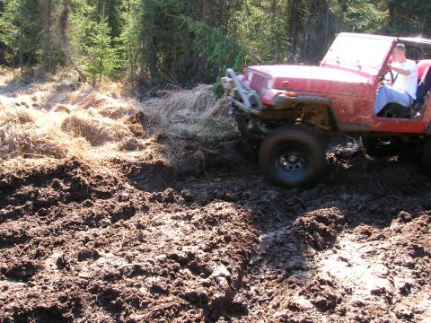 2003 Jeep TJ - A red Jeep Wrangler navigates a muddy trail in a wooded area.