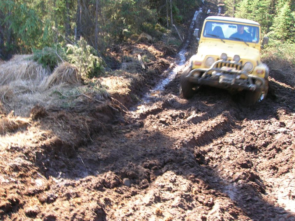 Yellow 2003 Jeep TJ navigating a muddy trail with trees in the background