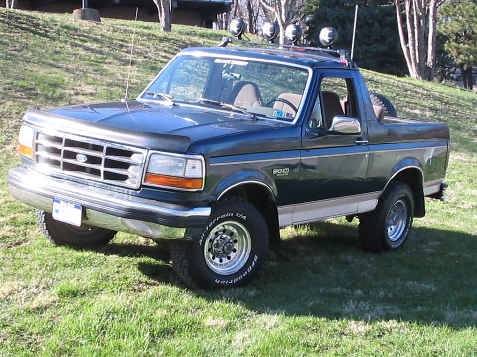 Dark green Ford Bronco with top removed, roof light bar and BFG All-Terrain tires on grass