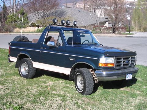 1992 Ford Bronco - Dark green 1992 Ford Bronco parked on a grassy lawn with a house in the background.
