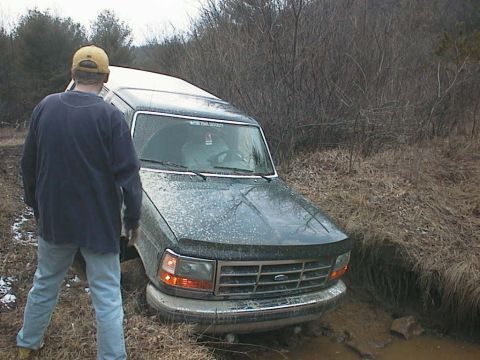 1992 Ford Bronco - A person observes a 1992 Ford Bronco that has become stuck in a muddy off-road area.