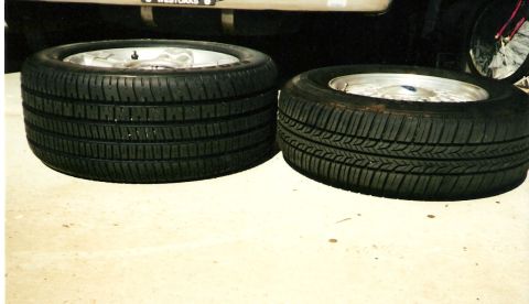 1992 Ford Crown Victoria - Two tires mounted on silver alloy wheels lying on their sides on a light concrete floor, showing noticeably different tread patterns and de…