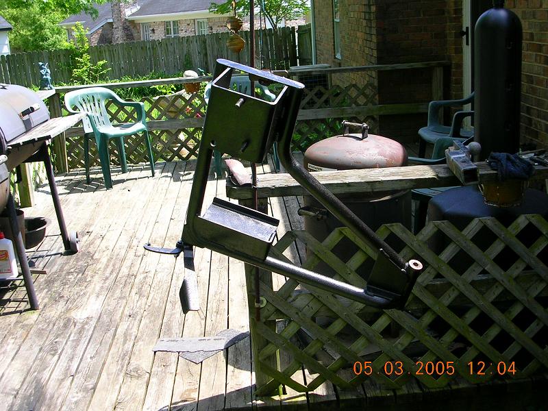 Metal bracket assembly on a wooden deck with a grill and chairs visible