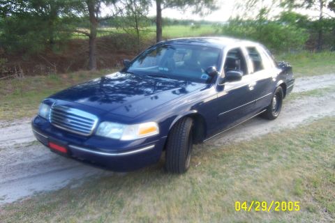 1998 Ford Crown Victoria - A dark blue sedan is parked on a dirt road with grass and trees surrounding it. The date 04/29/2005 is visible in the lower right corner.