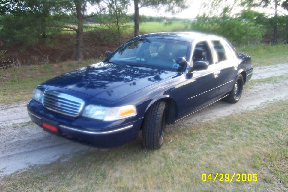 Dark blue Ford Crown Victoria on black steel wheels, front 3/4 view on a dirt track
