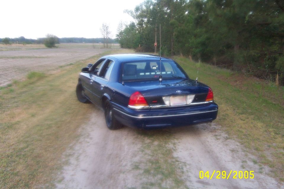 Dark blue Ford Crown Victoria sedan, rear three-quarter view, trunk whip antennas and deck lights