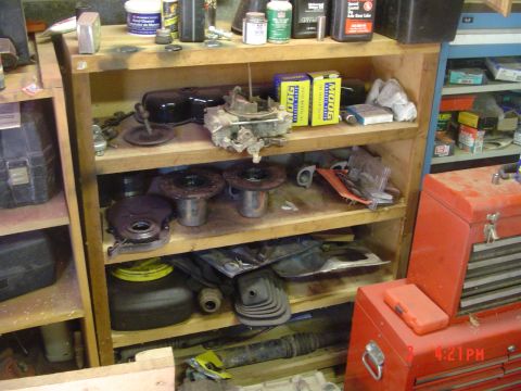 1985 Ford Bronco - A collection of automotive parts are organized on wooden shelves in a workshop setting.