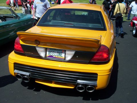 1998 Ford Crown Victoria - Rear view of a yellow sedan with a spoiler and custom exhaust. The license plate reads REELONE.