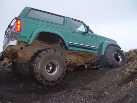 1996 Ford Bronco - This modified SUV is shown at an angle on a dark, sandy terrain under an overcast sky.