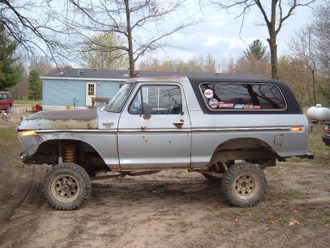 1979 Ford Bronco - This lifted Ford Bronco has a rusty hood and is parked on a dirt lot with a house in the background.