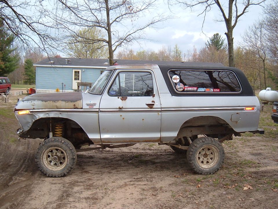 Silver Ford Bronco with lifted suspension and off-road tires. Hood is rusty and dented