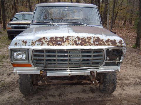 1979 Ford Bronco - A weathered 1978 Ford Bronco sits in a wooded area, showing significant rust and damage.