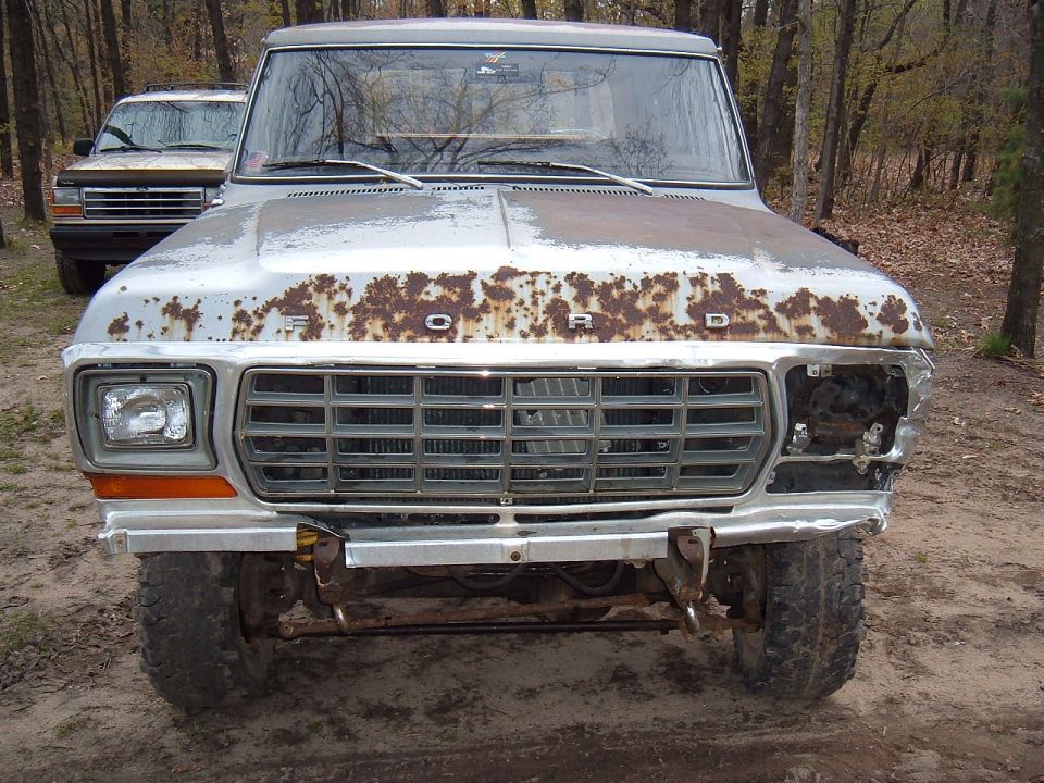 Rusty 1978 Ford Bronco front view, missing headlight, with another vehicle behind it