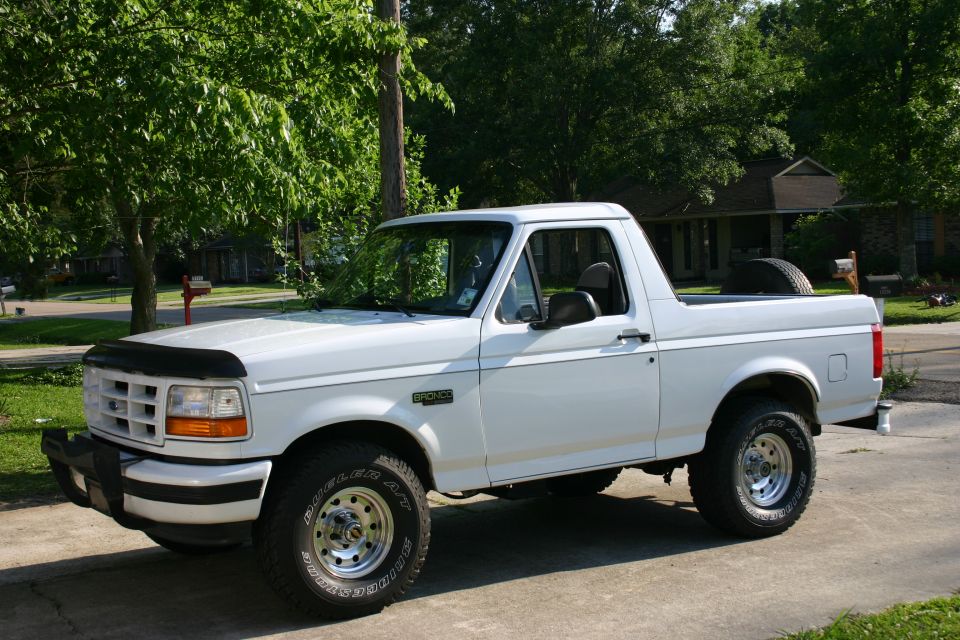 White Ford Bronco with rear top removed, chrome wheels and hood deflector, parked in a driveway
