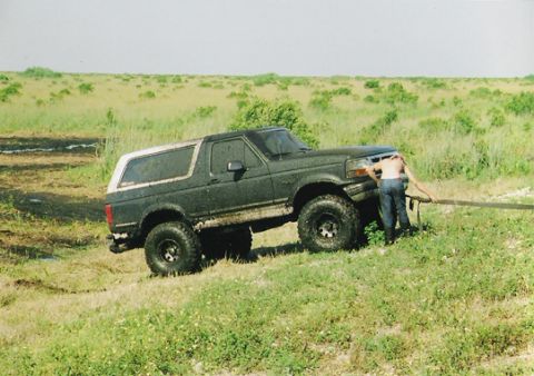 1992 Ford Bronco - A person attempts to free a mud-covered Ford Bronco from a grassy ditch.