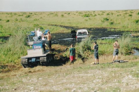 1992 Ford Bronco - Two vehicles are stuck in a muddy field with several people observing the situation.