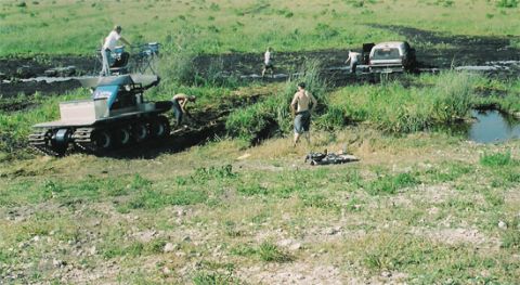 1992 Ford Bronco - People work around a tracked vehicle and a stuck SUV in a muddy, grassy area.